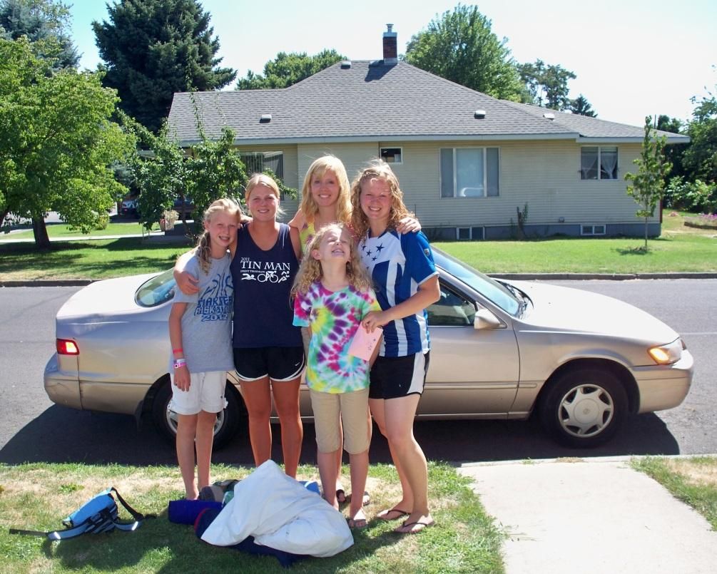 Photo from the 2012 Christmas letter: four girls standing beside a tan car in front of a house
